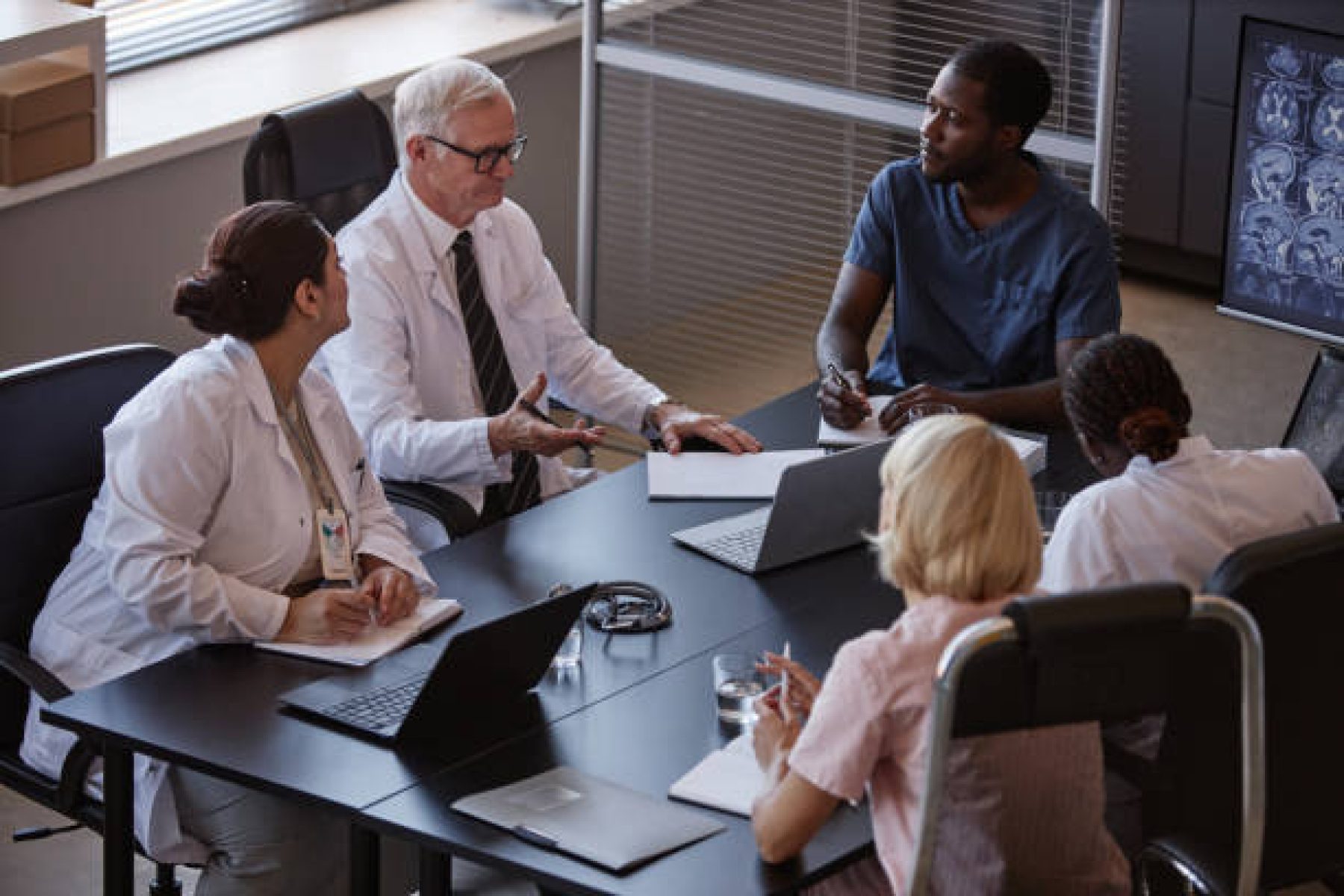 High angle shot of diverse group of professional clinicians thoroughly studying anamnesis of patients disease sitting at meeting table, while collaboratively planning treatment at medical office